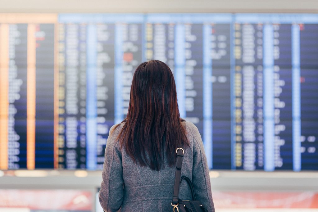 Woman looking up and checking the schedule from the Arrival Departure Board at airport terminal.